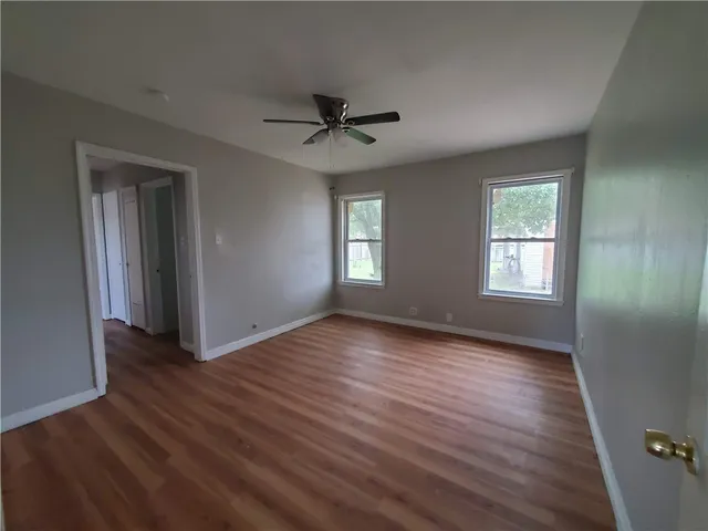 an empty room with wooden floor ceiling fan and windows