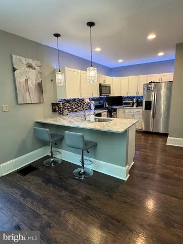 a room with stainless steel appliances kitchen island granite countertop a sink a stove and a wooden floors