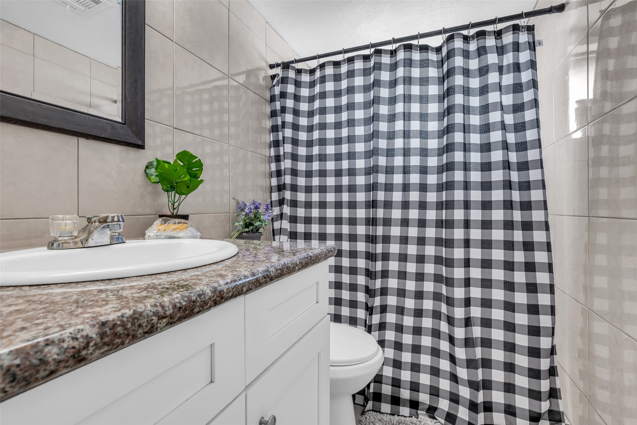 10730 Filey Lane Houston, TX 77013 - Photo 18 of 25 Cozy and modern bathroom featuring tiled walls, a granite countertop with a white vanity, and a stylish black-and-white checkered shower curtain.