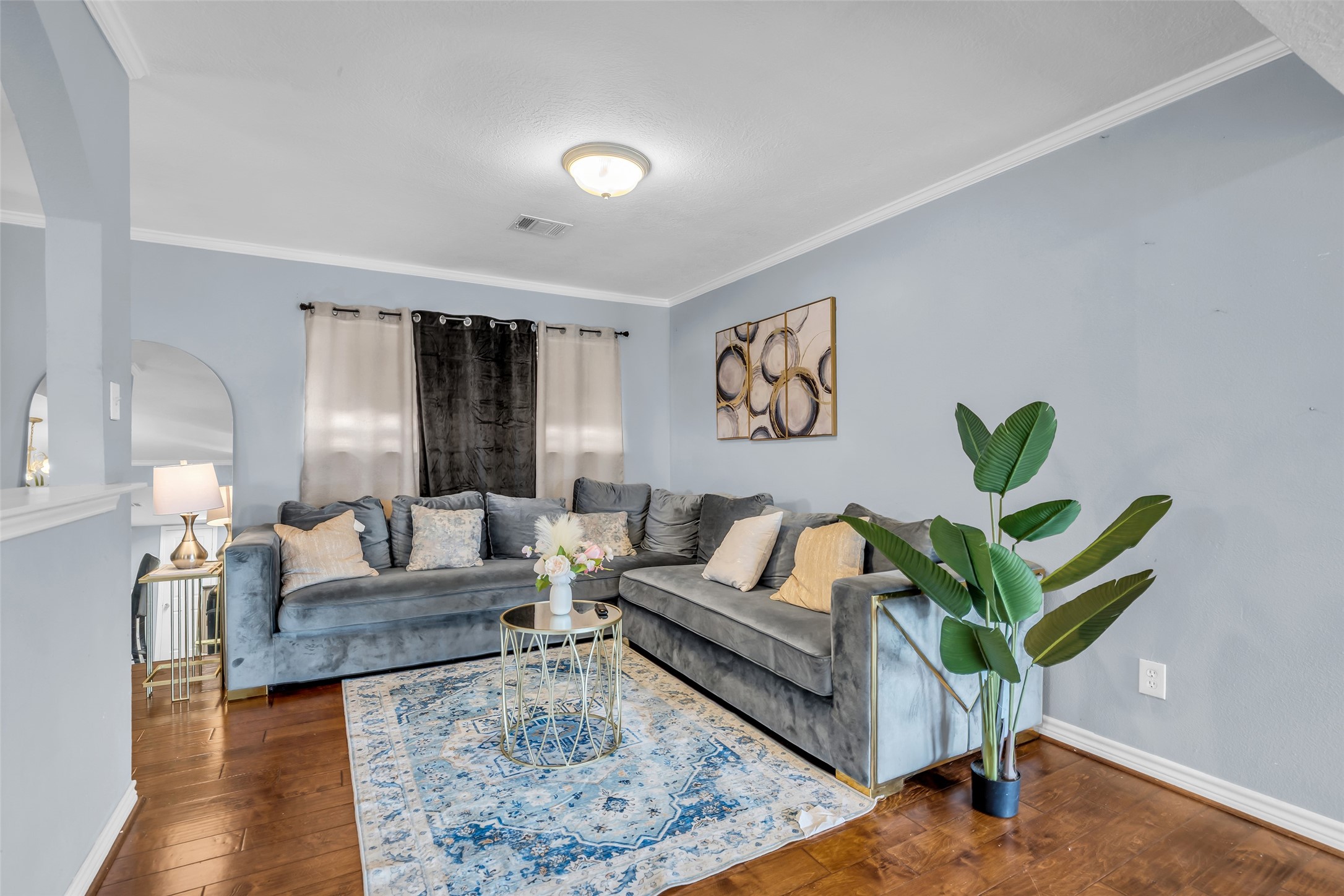 10730 Filey Lane Houston, TX 77013 - Photo 2 of 25 This inviting living room features gray/blue walls and a vibrant area rug complement the warm wooden floor, creating a welcoming and elegant atmosphere.