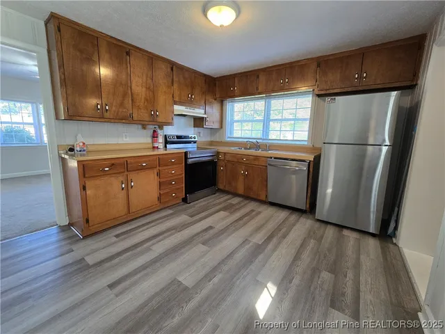 a kitchen with stainless steel appliances granite countertop a refrigerator a sink dishwasher a stove with wooden cabinets and floor