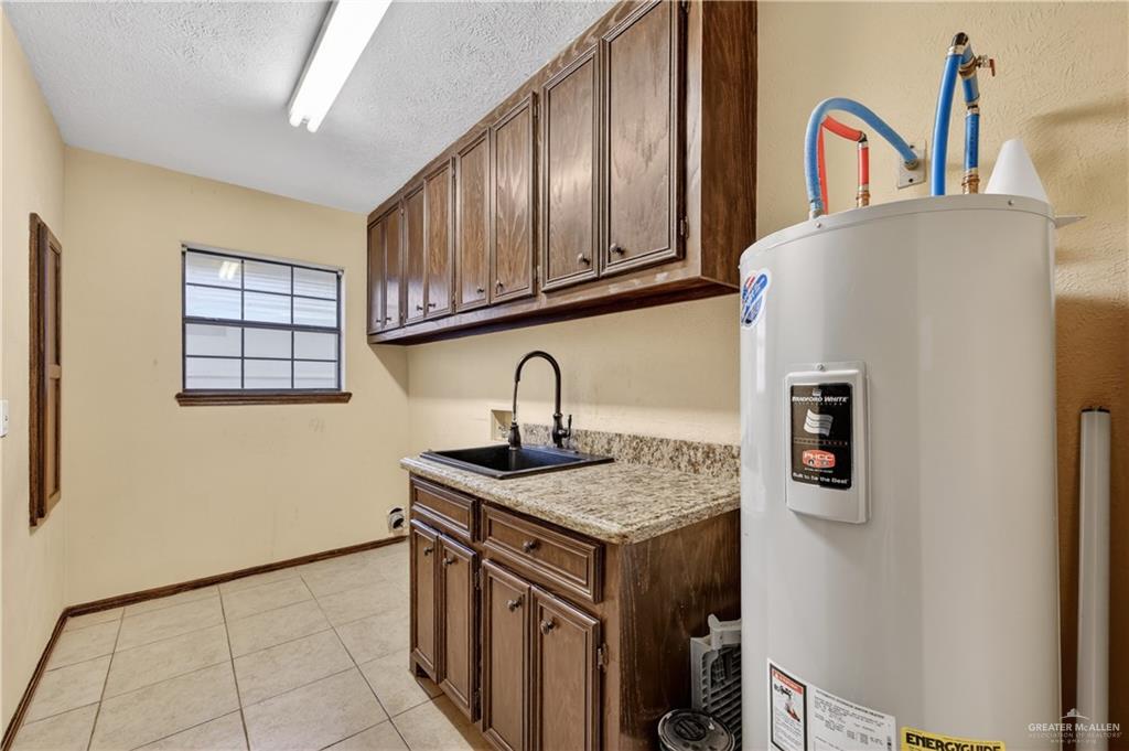 6004 North Cynthia Street McAllen, TX 78504 - Photo 13 of 25 Utility room featuring tile flooring, a built-in sink with a black faucet, granite-look countertops, and ample cabinetry
