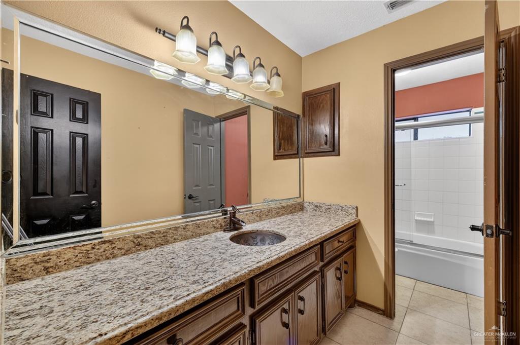 6004 North Cynthia Street McAllen, TX 78504 - Photo 18 of 25 Bathroom vanity featuring a speckled countertop, integrated sink, and traditional wood-finish cabinetry