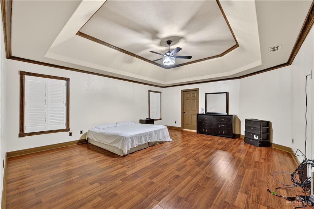 6004 North Cynthia Street McAllen, TX 78504 - Photo 19 of 25 Spacious room featuring wood-finish flooring, white walls, and a tray ceiling with dark wood trim