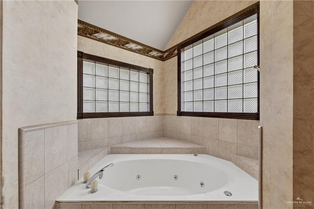 6004 North Cynthia Street McAllen, TX 78504 - Photo 21 of 25 Corner jetted tub set within a tiled surround, featuring dual glass block windows with dark wood trim and textured walls