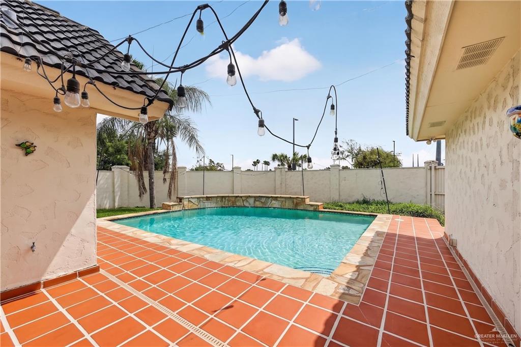6004 North Cynthia Street McAllen, TX 78504 - Photo 23 of 25 Outdoor swimming pool with integrated waterfall feature, surrounded by terracotta tile decking and a textured stucco exterior