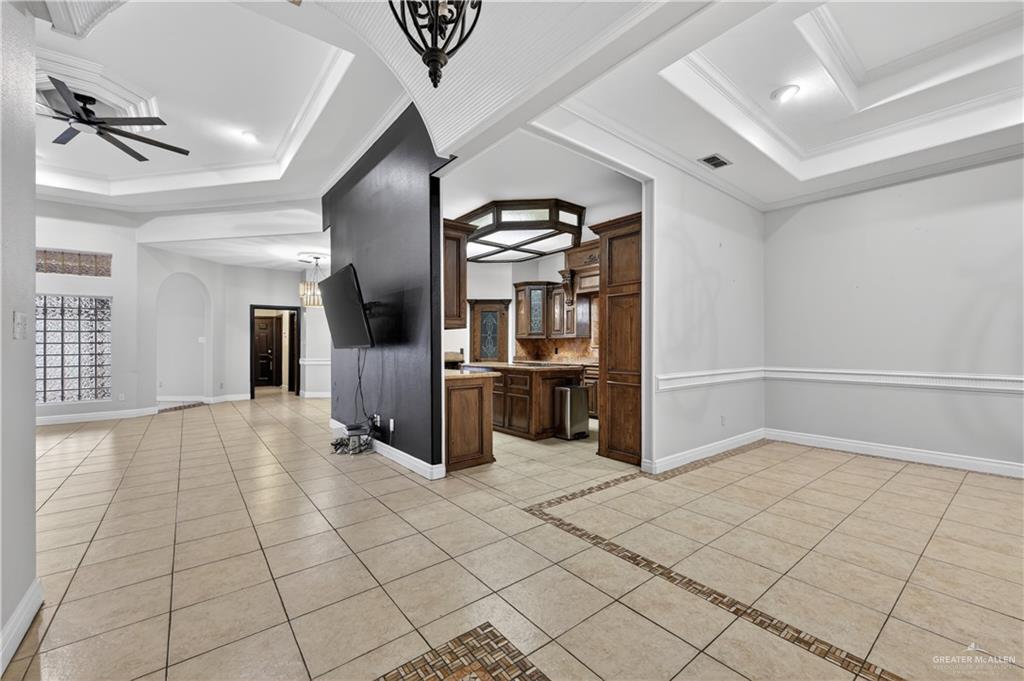6004 North Cynthia Street McAllen, TX 78504 - Photo 4 of 25 Spacious interior featuring light-toned tile flooring with decorative inlay, tray ceilings with crown molding, and a partial dark-painted accent wall