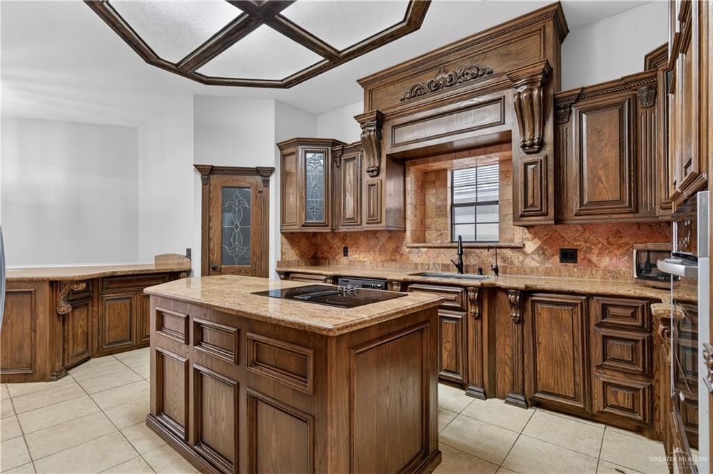 6004 North Cynthia Street McAllen, TX 78504 - Photo 7 of 25 Kitchen featuring custom wood cabinetry with ornate detailing, a central island with a built-in cooktop, and light-toned tile flooring