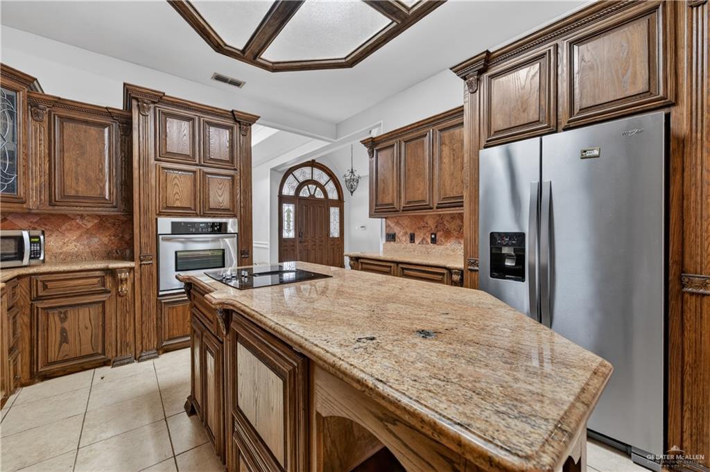 6004 North Cynthia Street McAllen, TX 78504 - Photo 9 of 25 Kitchen featuring an island with a built-in cooktop, extensive wood cabinetry, granite countertops, and stainless steel appliances