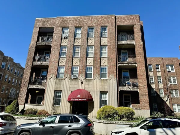 a front view of a building with lot of cars and trees