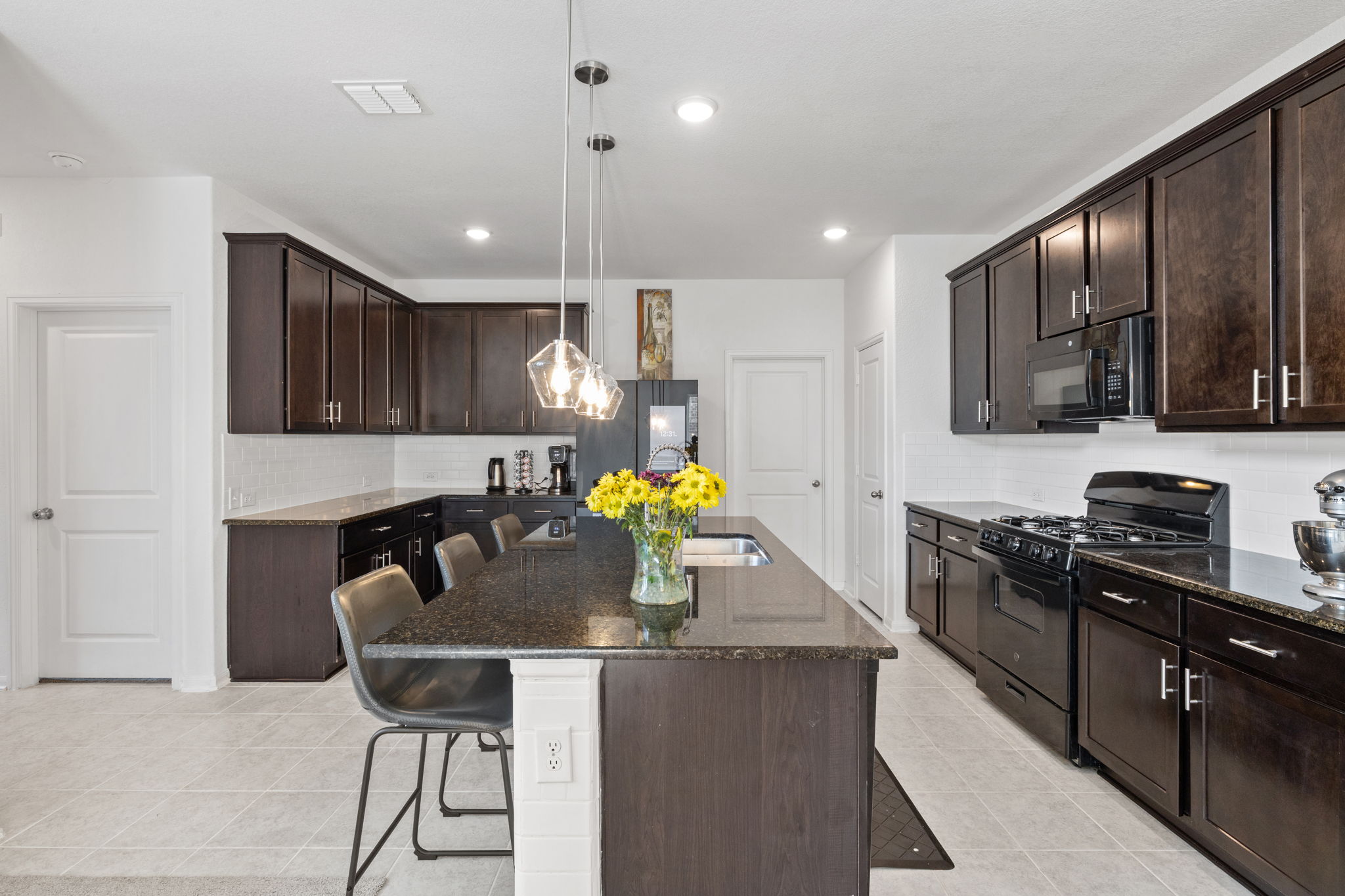 189 Durian Loop Buda, TX 78610 - Photo 12 of 38 Kitchen with a kitchen breakfast bar, black appliances, dark stone counters, dark brown cabinets, and a center island with sink