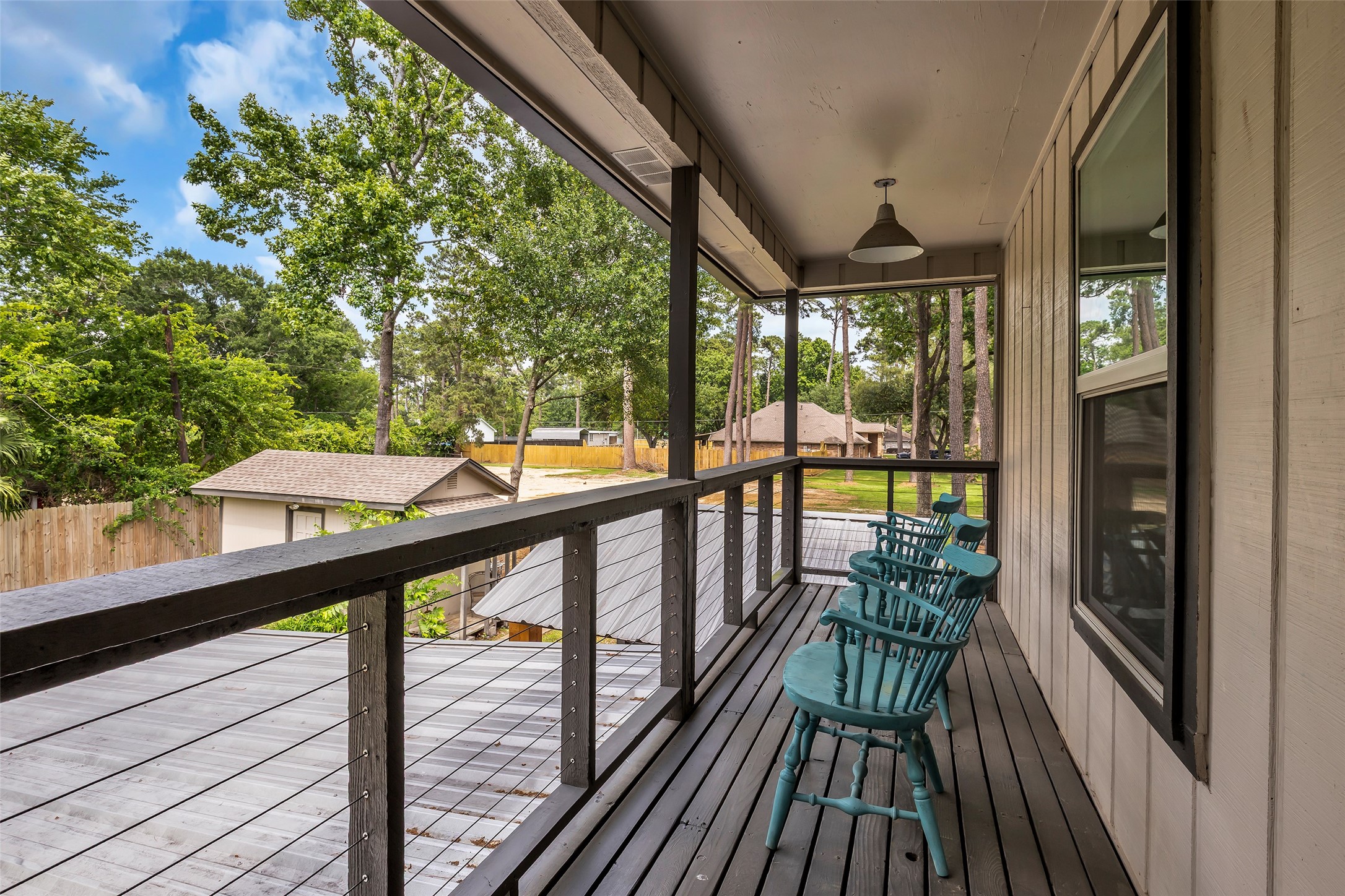 22502 Fields Lane Spring, TX 77389 - Photo 25 of 39 Cozy, covered balcony with a wooden railing and a row of blue chairs, offering a serene view of lush greenery.