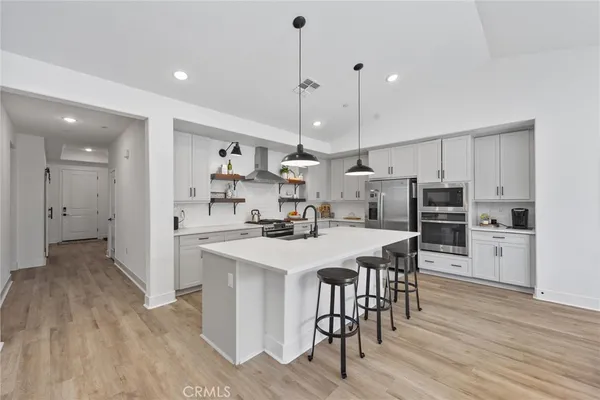 a kitchen with stainless steel appliances a stove a sink a refrigerator and white cabinets with wooden floor
