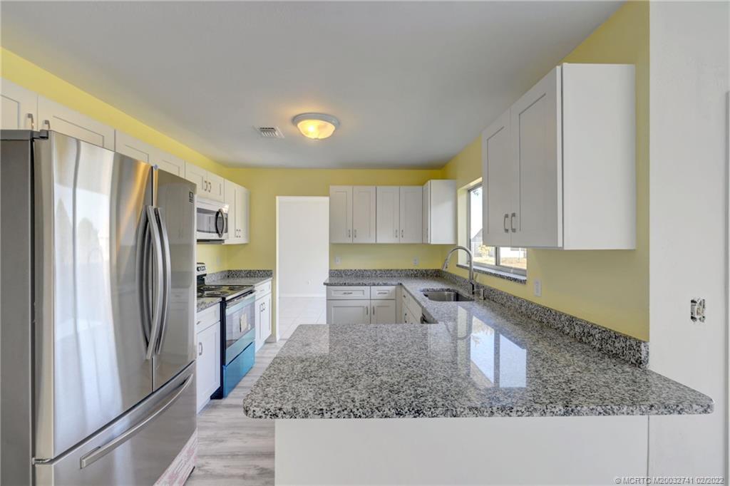 297 Southwest Homeland Road Port St. Lucie, FL 34953 - Photo 11 of 32 a kitchen with stainless steel appliances granite countertop a refrigerator a stove and a sink with wooden floor