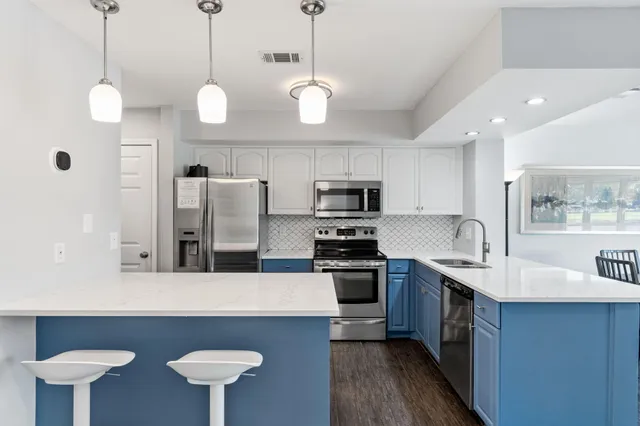 a kitchen with stainless steel appliances a stove a sink island and a refrigerator with wooden floor