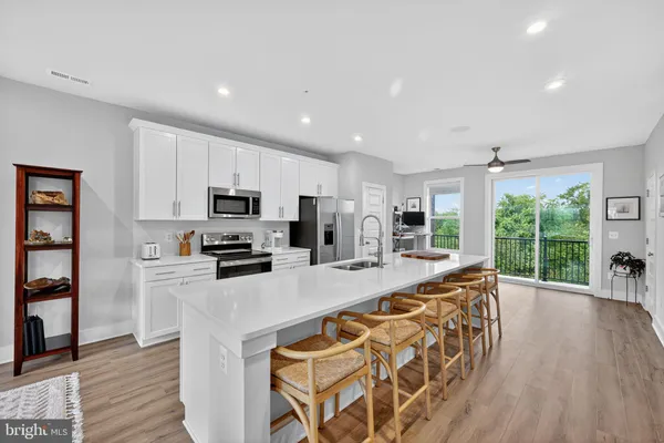 a kitchen with stainless steel appliances kitchen island granite countertop a refrigerator oven a sink dishwasher and white cabinets with wooden floor