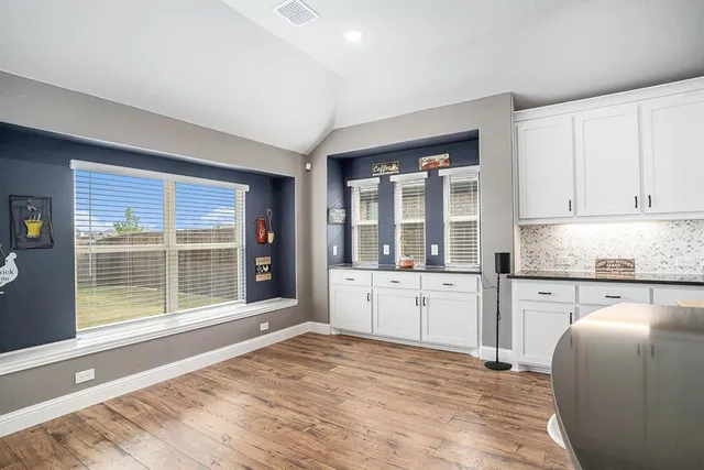 a large white kitchen with granite countertop a stove a sink a refrigerator and white cabinets with wooden floor