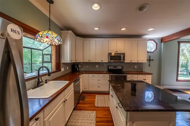 a kitchen with stainless steel appliances a microwave a stove a sink dishwasher a refrigerator and white cabinets with wooden floor