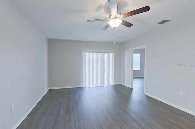 an empty room with wooden floor ceiling fan and window