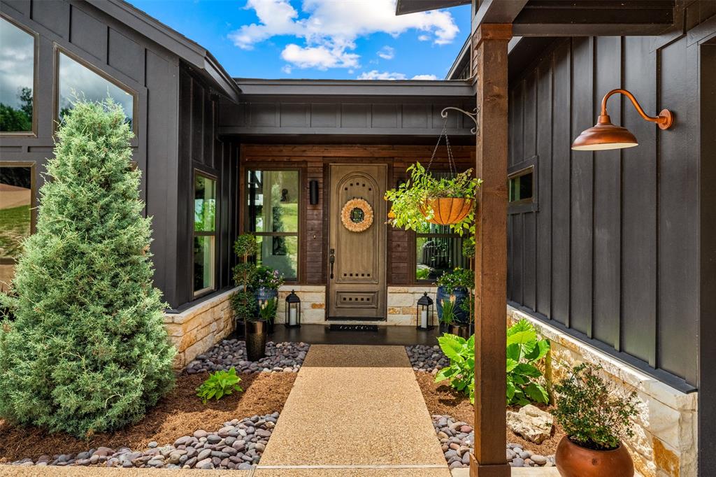 124 Bluffview Circle China Spring, TX 76633 - Photo 6 of 40 Inviting front entry featuring a stained wood door, board and batten siding, stone accents, a concrete walkway, and an arched outdoor light fixture