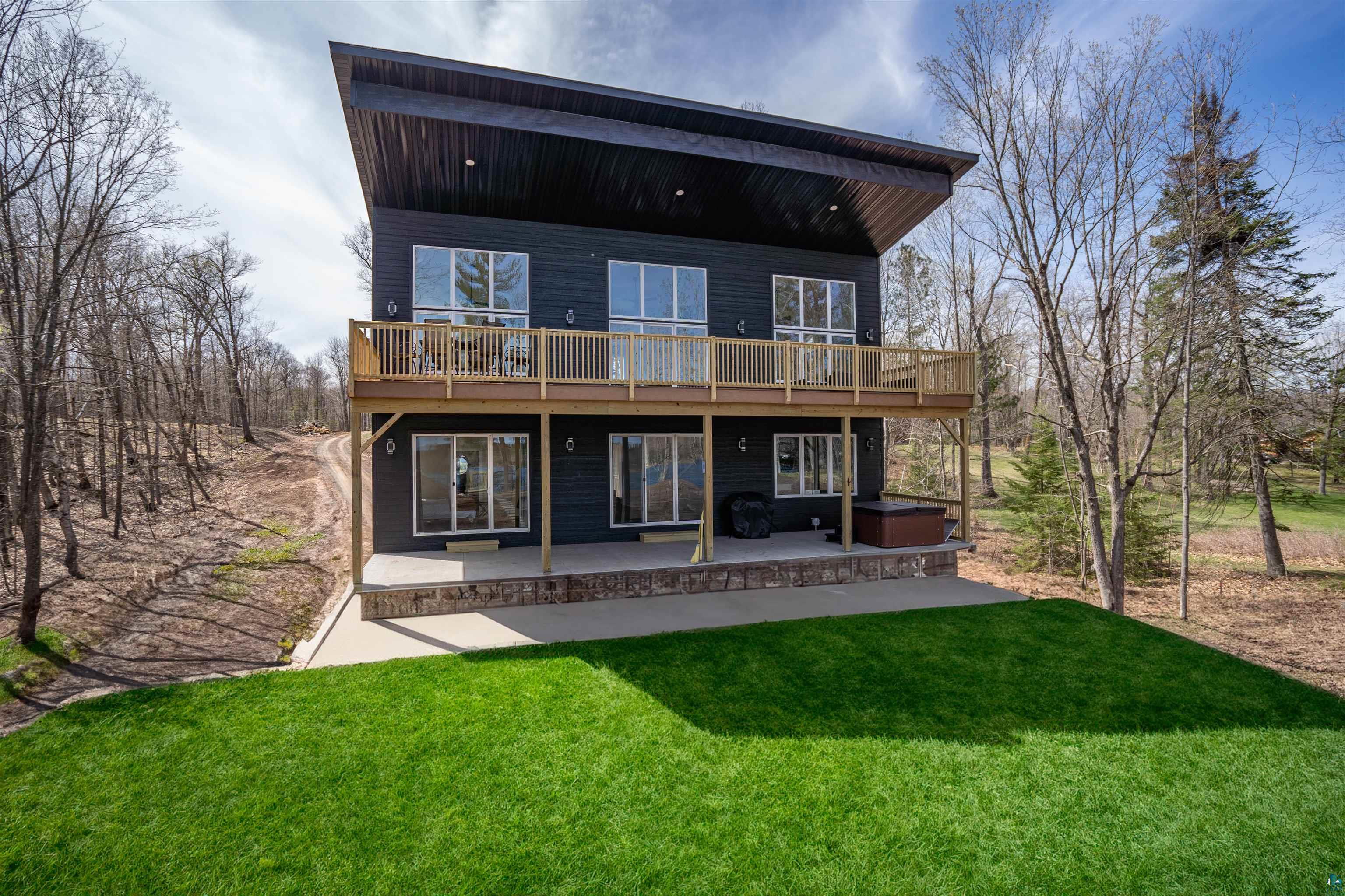 2000 West Chub Lake Road Carlton, MN 55718 - Photo 1 of 30 Modern exterior featuring dark horizontal siding, an expansive upper-level wood deck, and a concrete patio