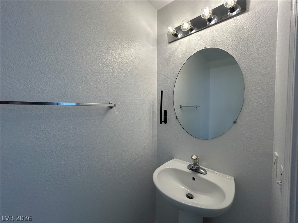 7373 Randel Jean Way Las Vegas, NV 89113 - Photo 7 of 14 A classic pedestal sink sits below a round mirror in this half bath.