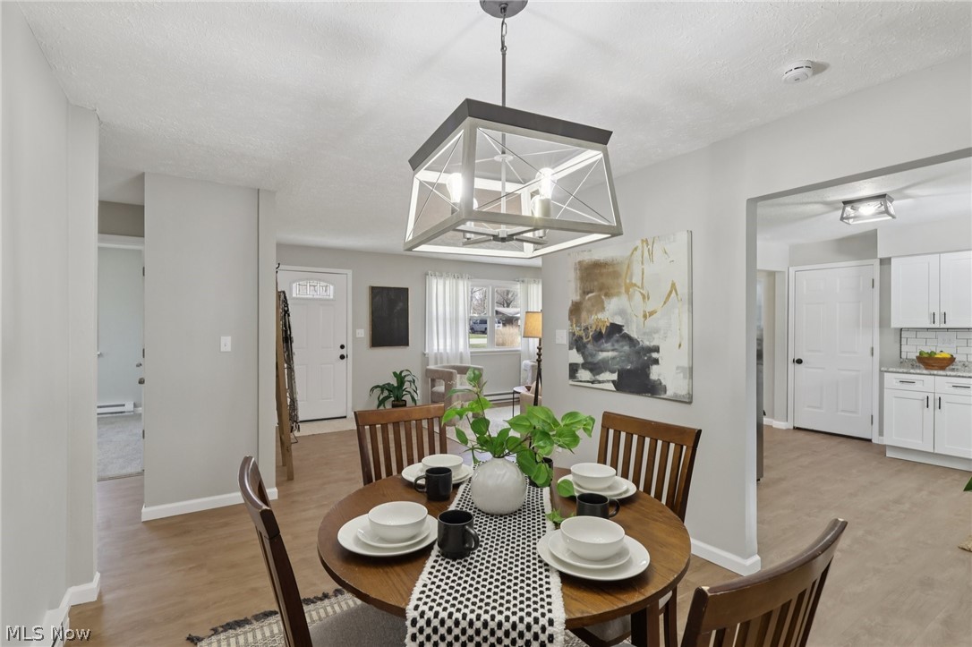 7412 Hopkins Road Mentor, OH 44060 - Photo 10 of 36 Dining space featuring light wood-style floors, a textured ceiling, baseboard heating, and suspended lighting