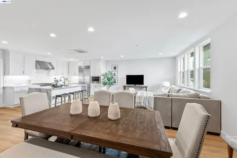 a kitchen with stainless steel appliances granite countertop a stove a refrigerator a sink a dining table and chairs with wooden floor