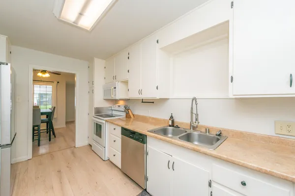 a kitchen with a sink dishwasher and white cabinets with wooden floor