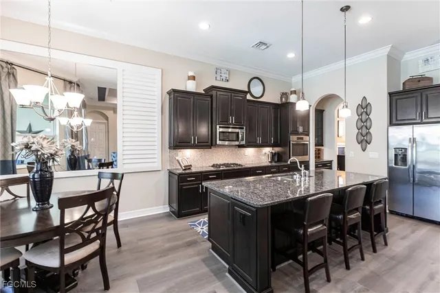 a kitchen with stainless steel appliances granite countertop a stove top oven a refrigerator a sink and chairs