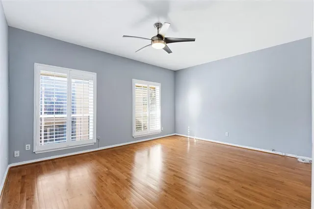 an empty room with wooden floor chandelier fan and windows