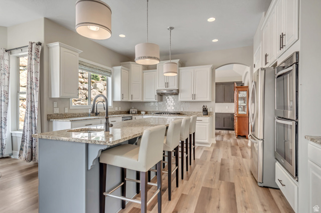 2543 East 700 South Springville, UT 84663 - Photo 29 of 73 Two tone kitchen with light stone countertops, a center island with sink, a kitchen bar, stainless steel appliances, and pendant lighting