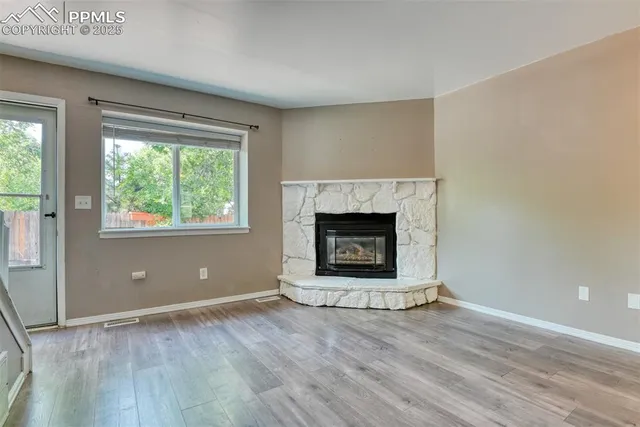 an empty room with wooden floor fireplace and windows