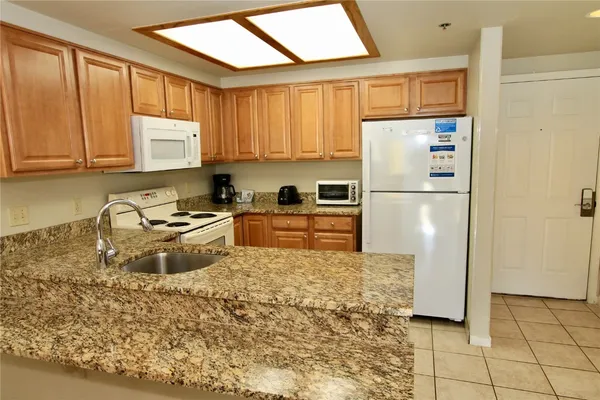 a kitchen with granite countertop a refrigerator a stove a sink dishwasher and wooden cabinets