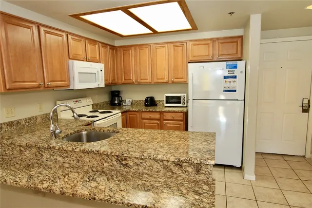 a kitchen with granite countertop a refrigerator a stove a sink dishwasher and wooden cabinets
