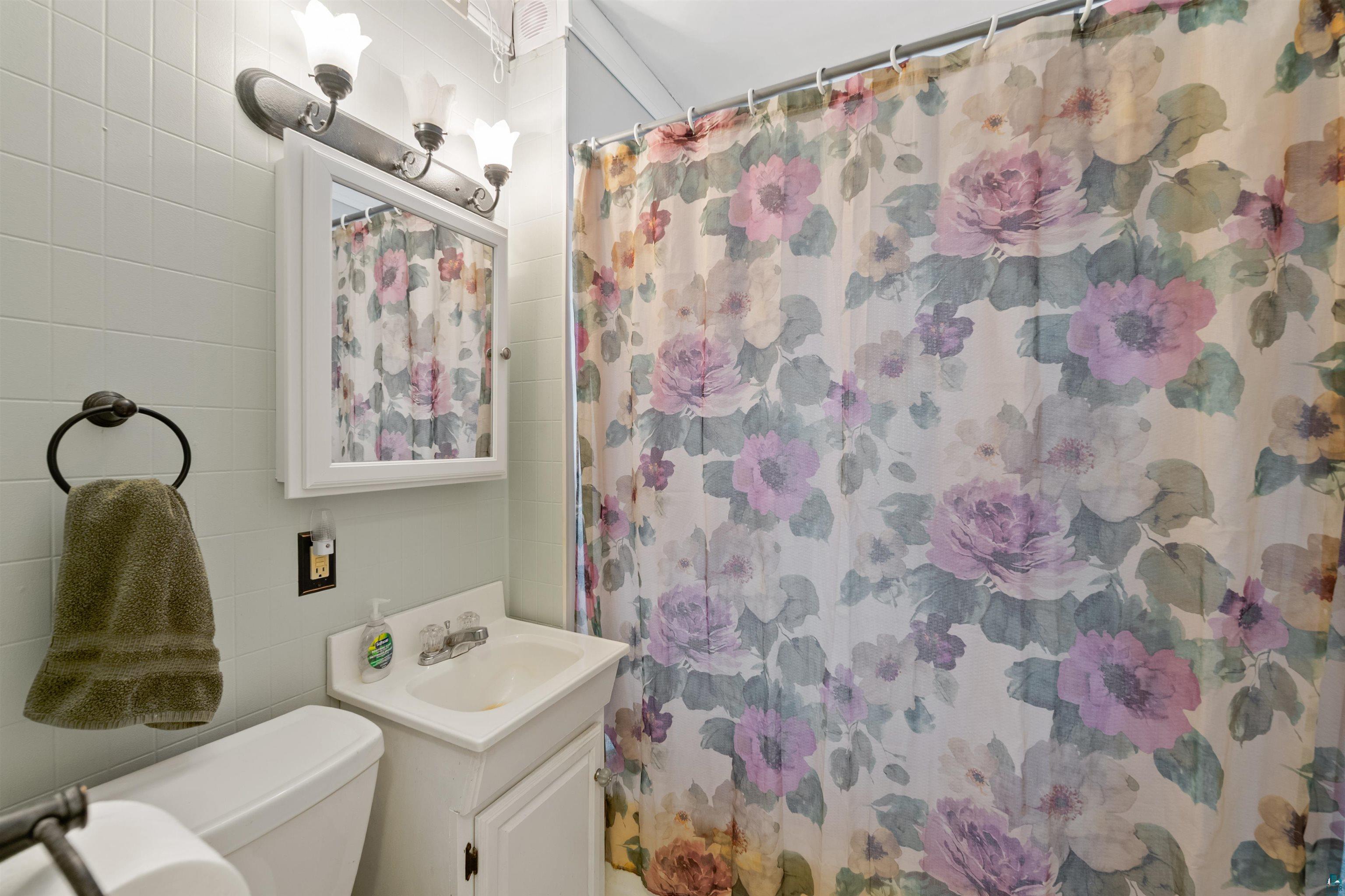 3209 Chestnut Street Duluth, MN 55806 - Photo 13 of 28 Full bathroom featuring a white vanity with integrated sink, coordinating wall-mounted medicine cabinet, and three-light vanity fixture