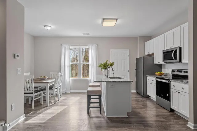 a kitchen with stainless steel appliances kitchen island granite countertop a stove a sink a refrigerator a dining table and chairs with wooden floor