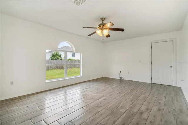 an empty room with wooden floor fan and windows