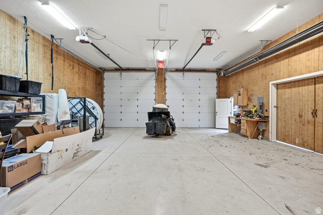 672 Perry Hollow Drive Mapleton, UT 84664 - Photo 85 of 106 Spacious garage featuring two overhead doors with automatic openers, wood-panel walls, and a built-in workbench with cabinetry