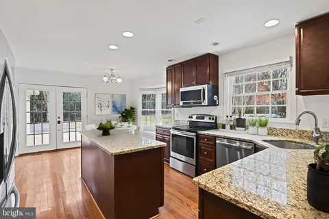 a open kitchen with granite countertop a sink dishwasher stove top oven and cabinets with wooden floor