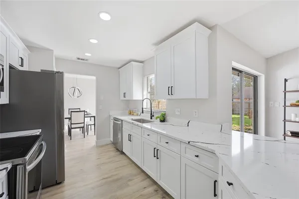 a large kitchen with stainless steel appliances granite countertop a refrigerator a sink dishwasher and white cabinets with wooden floor