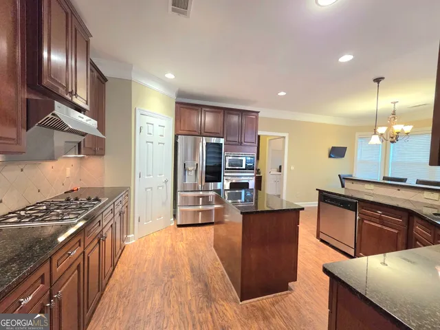 a kitchen with stainless steel appliances kitchen island granite countertop a stove refrigerator and cabinets