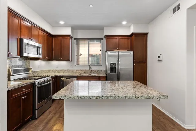 a kitchen with stainless steel appliances granite countertop a stove top oven a sink dishwasher a microwave oven and a stove with wooden floor