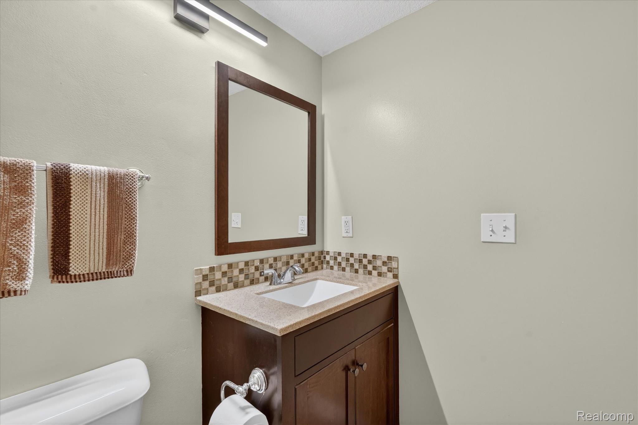 456 Lilly View Court Howell, MI 48843 - Photo 18 of 45 Bathroom vanity featuring a wood-finish cabinet, light countertop, and square mosaic tile backsplash