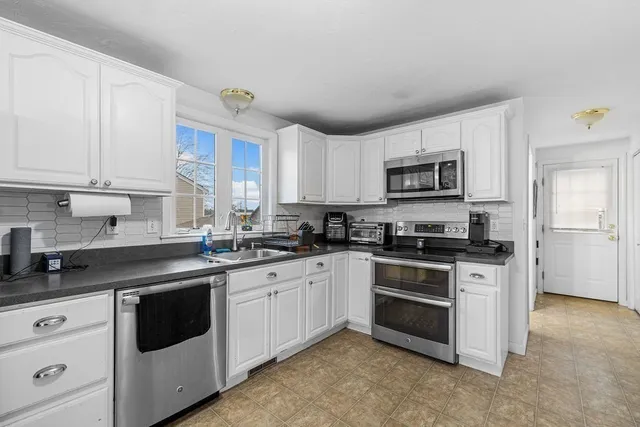 a kitchen with stainless steel appliances granite countertop white cabinets a sink a stove a microwave and a refrigerator