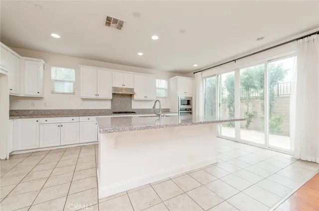 a large kitchen with stainless steel appliances granite countertop a stove a sink and white cabinets