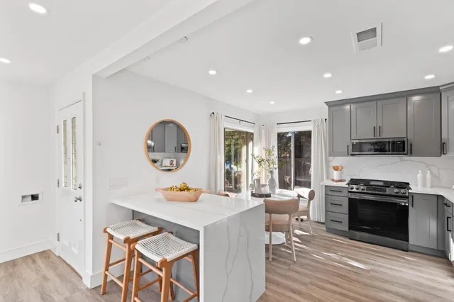 a kitchen with stainless steel appliances granite countertop a stove top oven a sink dishwasher and a dining table with wooden floor