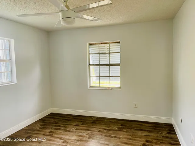 an empty room with wooden floor window and ceiling fan