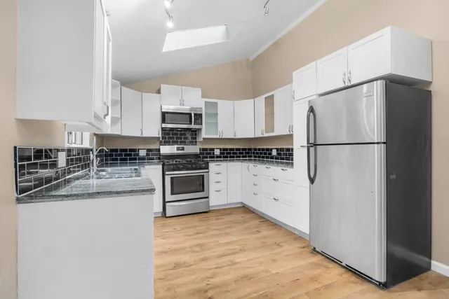 a kitchen with granite countertop a refrigerator sink stove and white cabinets