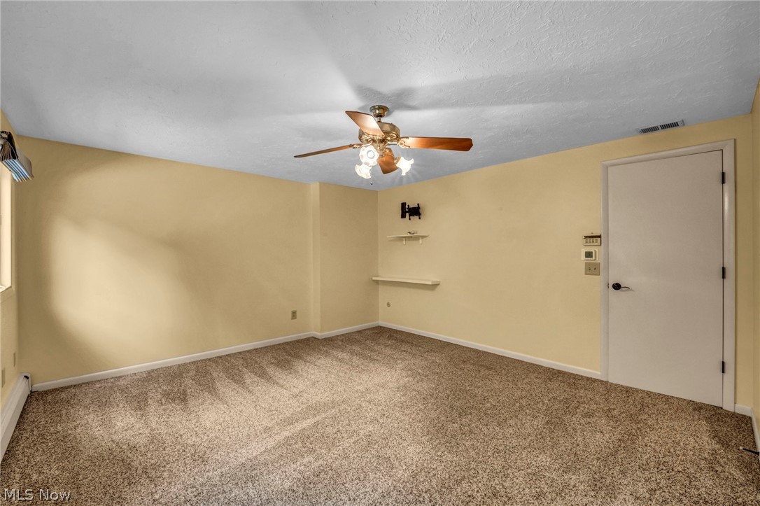 6845 Liberty Road Solon, OH 44139 - Photo 24 of 47 Carpeted room featuring a ceiling fan with integrated lighting, a wall-mounted television bracket, two white floating shelves, a white door with black hardware, and a window with white trim